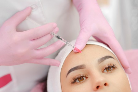 Woman gets injection in her face. Beauty woman giving botox injections. Young woman gets beauty facial injections in the cosmetology salon. Face aging injection. Aesthetic Medicine, Cosmetologyの写真素材