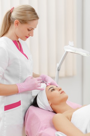 Woman gets injection in her face. Beauty woman giving botox injections. Young woman gets beauty facial injections in the cosmetology salon. Face aging injection. Aesthetic Medicine, Cosmetologyの写真素材