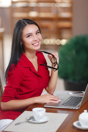 Businesswoman Working On Laptop In Coffee Shop. Young business woman uses laptop in cafe. Businesswoman looking at the cameraの写真素材