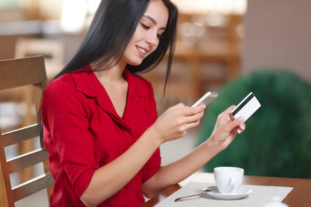 Young business woman holding mobile phone and credit card. Woman pays for a purchase with credit card. Purchase and shopping online.の写真素材