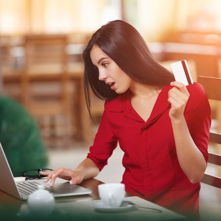 Angered woman holding credit card and looks in laptop screen. Purchase on the Internet. Buy online. Shopping onlineの写真素材