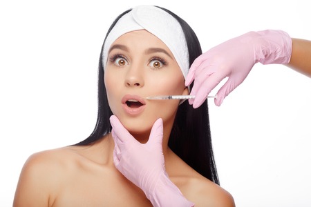 Astonished young woman gets injection in her lips. Close-up woman hyaluronic acid injection in lips. Injections of skin rejuvenation. Cosmetic procedures, injections, hyaluronic acid.の写真素材