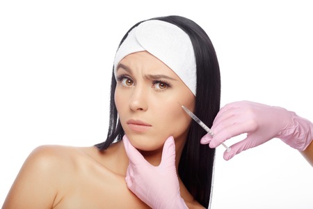 Astonished woman getting lifting injection in cheekbones. Close-up woman hyaluronic acid injection. Injections of skin rejuvenation. Cosmetic procedures, injections, hyaluronic acid.の写真素材