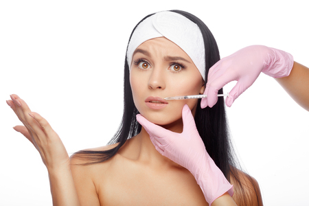 Frightened young woman gets injection in her lips. Close-up woman hyaluronic acid injection in lips. Injections of skin rejuvenation. Cosmetic procedures, injections, hyaluronic acid.の写真素材