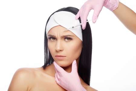 Astonished woman getting lifting injection in cheekbones. Close-up woman hyaluronic acid injection. Injections of skin rejuvenation. Cosmetic procedures, injections, hyaluronic acid.の写真素材
