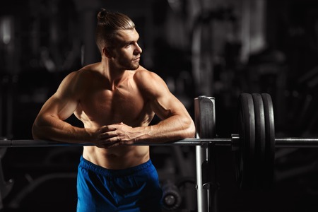 Attractive muscular bodybuilder guy prepare to do exercises with barbell in a gym. Guy bodybuilder tired in gym. Young Man Bodybuilder Resting In Gym After Exercisingの写真素材