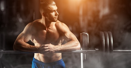 Attractive muscular bodybuilder guy prepare to do exercises with barbell in a gym. Guy bodybuilder tired in gym. Young Man Bodybuilder Resting In Gym After Exercisingの写真素材