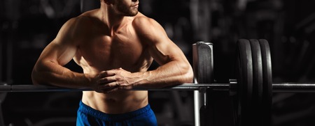 Attractive muscular bodybuilder guy prepare to do exercises with barbell in a gym. Guy bodybuilder tired in gym. Young Man Bodybuilder Resting In Gym After Exercisingの写真素材