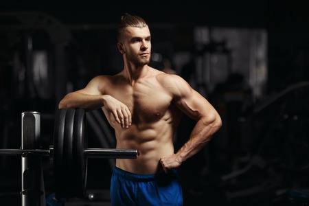Attractive muscular bodybuilder guy prepare to do exercises with barbell in a gym. Guy bodybuilder tired in gym. Young Man Bodybuilder Resting In Gym After Exercisingの写真素材
