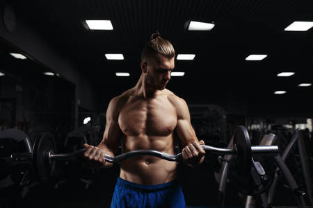 Muscular man working out in gym doing exercises with barbell at biceps, strong male naked torso abs. Muscular bodybuilder doing exercise with barbell. Bodybuilder in the gymの写真素材