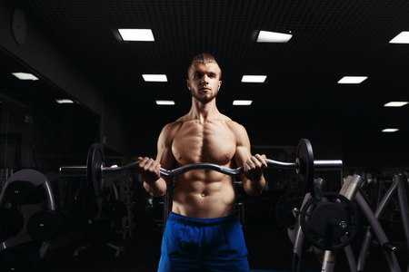 Muscular man working out in gym doing exercises with barbell at biceps, strong male naked torso abs. Muscular bodybuilder doing exercise with barbell. Bodybuilder in the gymの写真素材
