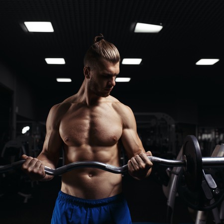 Muscular man working out in gym doing exercises with barbell at biceps, strong male naked torso abs. Muscular bodybuilder doing exercise with barbell. Bodybuilder in the gymの写真素材