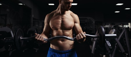 Muscular man working out in gym doing exercises with barbell at biceps, strong male naked torso abs. Muscular bodybuilder doing exercise with barbell. Bodybuilder in the gymの写真素材