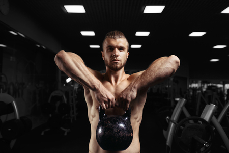 Fitness man doing a weight training by lifting heavy kettlebell. Yong athlete doing kettlebell swings. Bodybuilder lifting kettlebellの写真素材