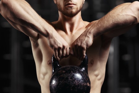 Fitness man doing a weight training by lifting heavy kettlebell. Yong athlete doing kettlebell swings. Bodybuilder lifting kettlebellの写真素材