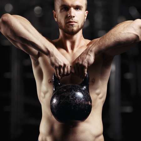 Fitness man doing a weight training by lifting heavy kettlebell. Yong athlete doing kettlebell swings. Bodybuilder lifting kettlebellの写真素材