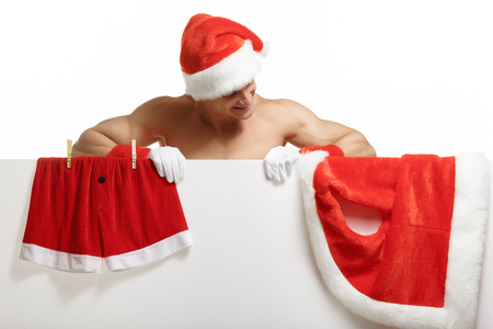 Santa Claus muscular hung his clothes on a banner sales. Sexy Santa Claus. Muscular Santa Claus on a white backgroundの写真素材