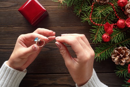 Christmas background. Engagement ring in female hands among Christmas decorations on wood background. Romance, jewelry concept - woman hands with wedding ring in gift box. Gift on Valentine's Dayの写真素材