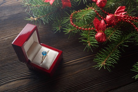 Christmas wooden background with Christmas tree and red ornaments. Christmas background with red wooden box. A Christmas gift. Gift on Valentine's Day. Jewelry red wooden box. Ring with blue gemの写真素材