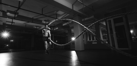 Fitness man working out with battle ropes at gym. Battle ropes fitness man at gym workout exercise fitted body. Fitness man training with battle rope in fitness club. Training with battle ropeの写真素材