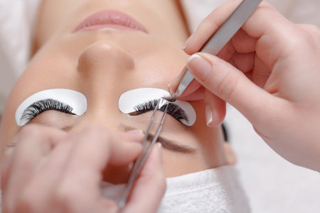 Permanent makeup. Eyelash Extension Procedure. Woman Eye with Long Eyelashes. Professional stylist...