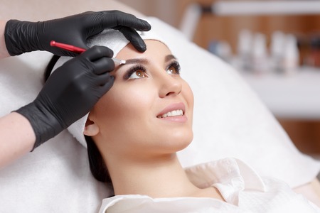 Permanent makeup eyebrows. Mikrobleyding eyebrows workflow in a beauty salon. Cosmetologist applying a special permanent makeup on a woman's eyebrows.の写真素材