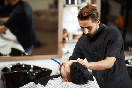 Hairstylist in black suite shaving and cutting bread of client.の写真素材