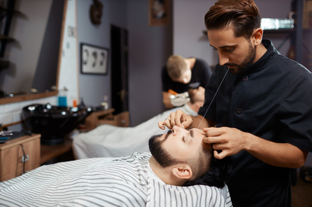 Brunet man visiting barbershop for  cutting beard of thread.の写真素材