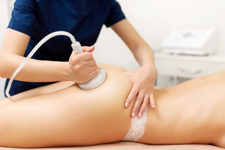 Cosmetology specialist massaging buttocks of naked woman using massage machine.の写真素材