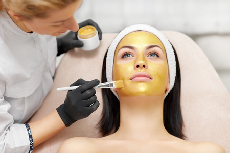 Applying of gold facial mask on skin of beautiful brunette.の写真素材