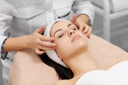 Beautician doing face massage to beautiful brunette.