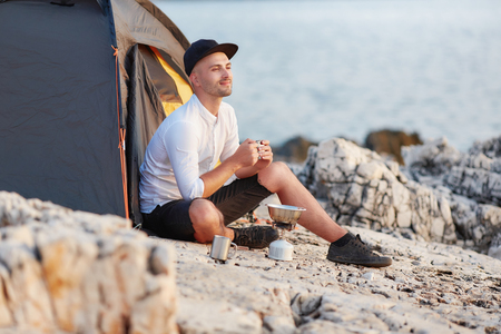 Man sitting with an iron cup on rocky coast of sea.の写真素材