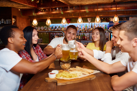 International group of friends celebrating with toast and clink raising glasses with beer.の写真素材