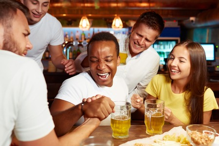 Excited male friends having arm wrestling challenge at local bar.の写真素材