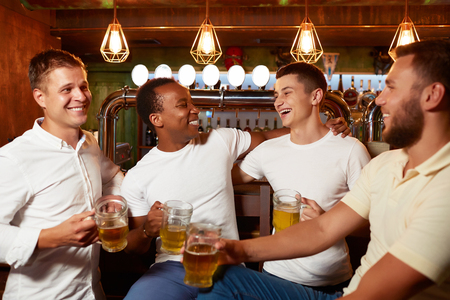 Company of four handsome men holding glass of beer, smiling and embracing.の写真素材