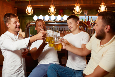 Four handsome men drinking beer together at pub clinking glasses.の写真素材