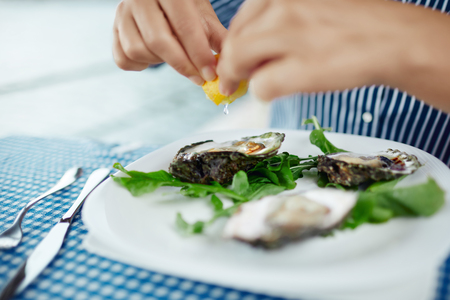 Womens hands squeezing lemon juice on raw oyster, close upの写真素材