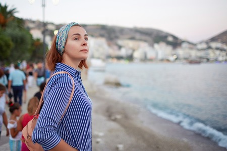 Young hipster woman enjoying sun and good warm day during her recreation time, female looking at the landscape while sitting near sea portの写真素材