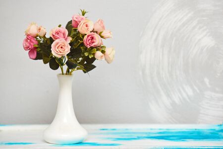 A sprig of artificial flowers stands in a white ceramic vase against a wallの写真素材