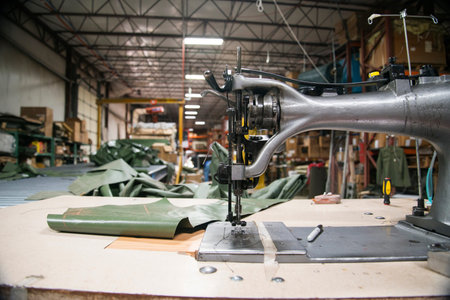 Industrial sewing machine used to sew tents on factory floor with scraps of material and marker on...