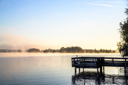 Misty Morning Lake with Autumn Colored Trees, Foliage, and Dockの写真素材