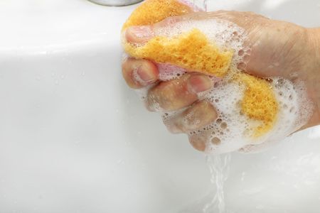 sponge for cleaning  in hand under running waterの写真素材