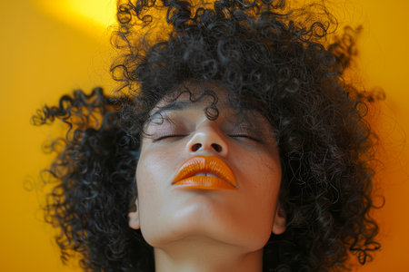 Close-up of a woman with voluminous curly hair and freckles, eyes closed, basking in the sunlight against a vivid yellow background.の素材