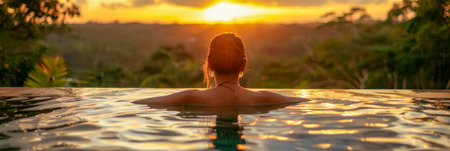 A woman is sitting in a pool as the sun sets in the background. She is relaxed and enjoying the peaceful atmosphere created by the beautiful sunset.の素材