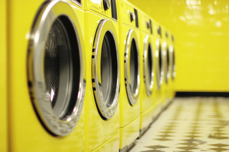 Bright Yellow Laundromat Interior with Modern Washing Machines in a Row.の素材