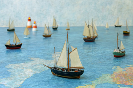Miniature Sailboats Navigating a Map with Lighthouses in the Background.の素材