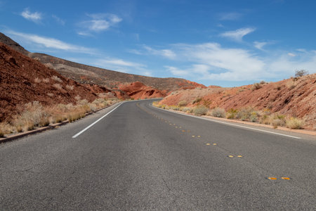 View of red sand and rock formations from a paved road in Nevada