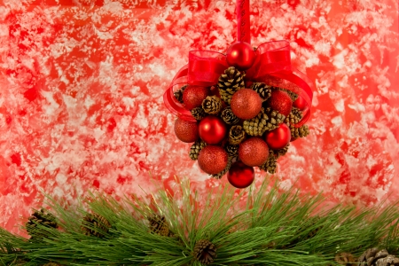 A pine cone and red ball hanging decoration with a red organza bow hangs above pine tree greens with pine cones.の写真素材