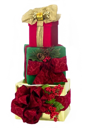 A gold foil-wrapped gift topped by a red damask bow, a green-wrapped gift topped by a red damask bow and a red damask gift topped by gold paper ribbons and bow are stacked one upon another.の写真素材
