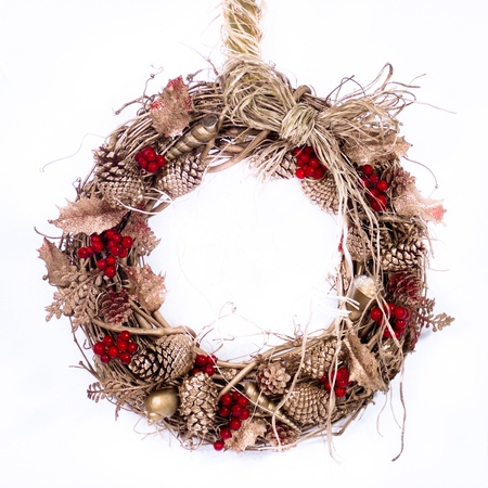 A natural twig wreath is decorated with pine cones, red berries, gold shells and a raffia bow の写真素材
